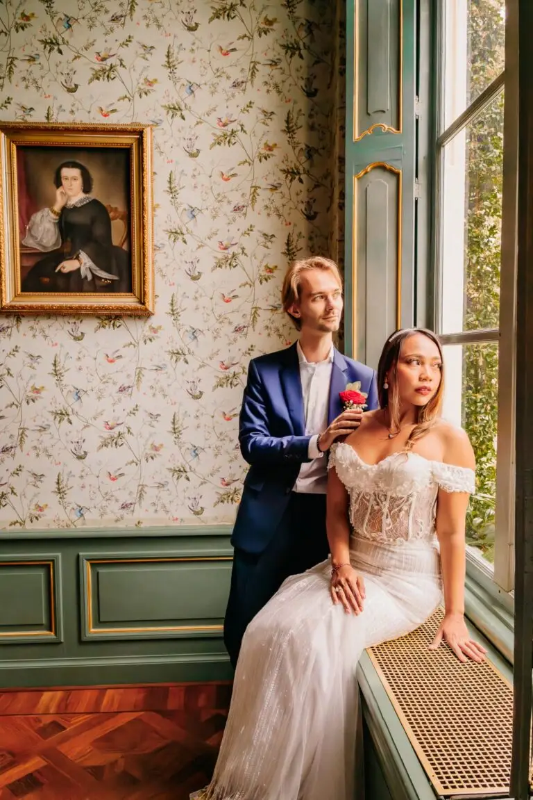 Bruidspaar bij een raam met een rode roos, sfeervolle bruidsfotografie door Indra Hunze