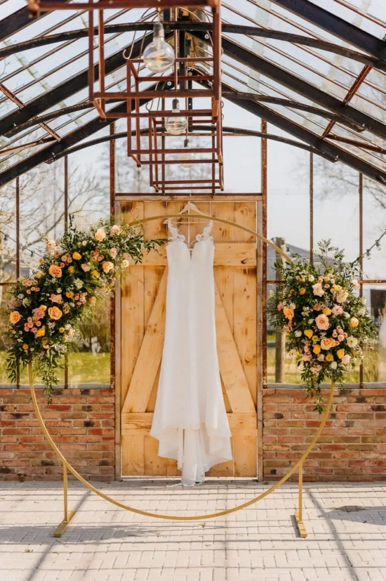 Trouwjurk in een kas met bloemenboog, sfeervolle bruiloftsdetails door Indra Hunze