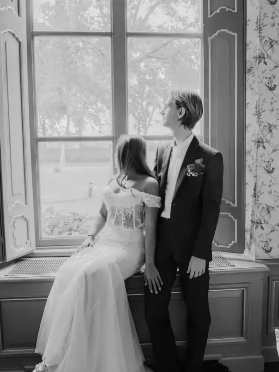 Bruidspaar bij een groot raam in zwart-wit, elegante bruidsfotografie door Indra Hunze