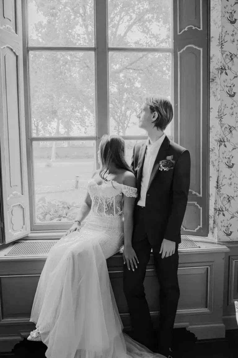 Bruidspaar bij een groot raam in zwart-wit, elegante bruidsfotografie door Indra Hunze