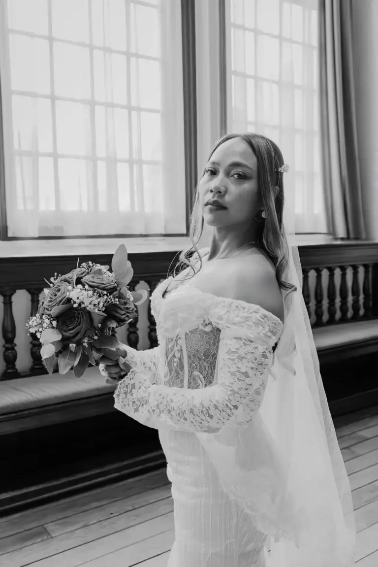 Bruid met bruidsboeket bij het raam, zwart-wit, bruiloftsfotografie